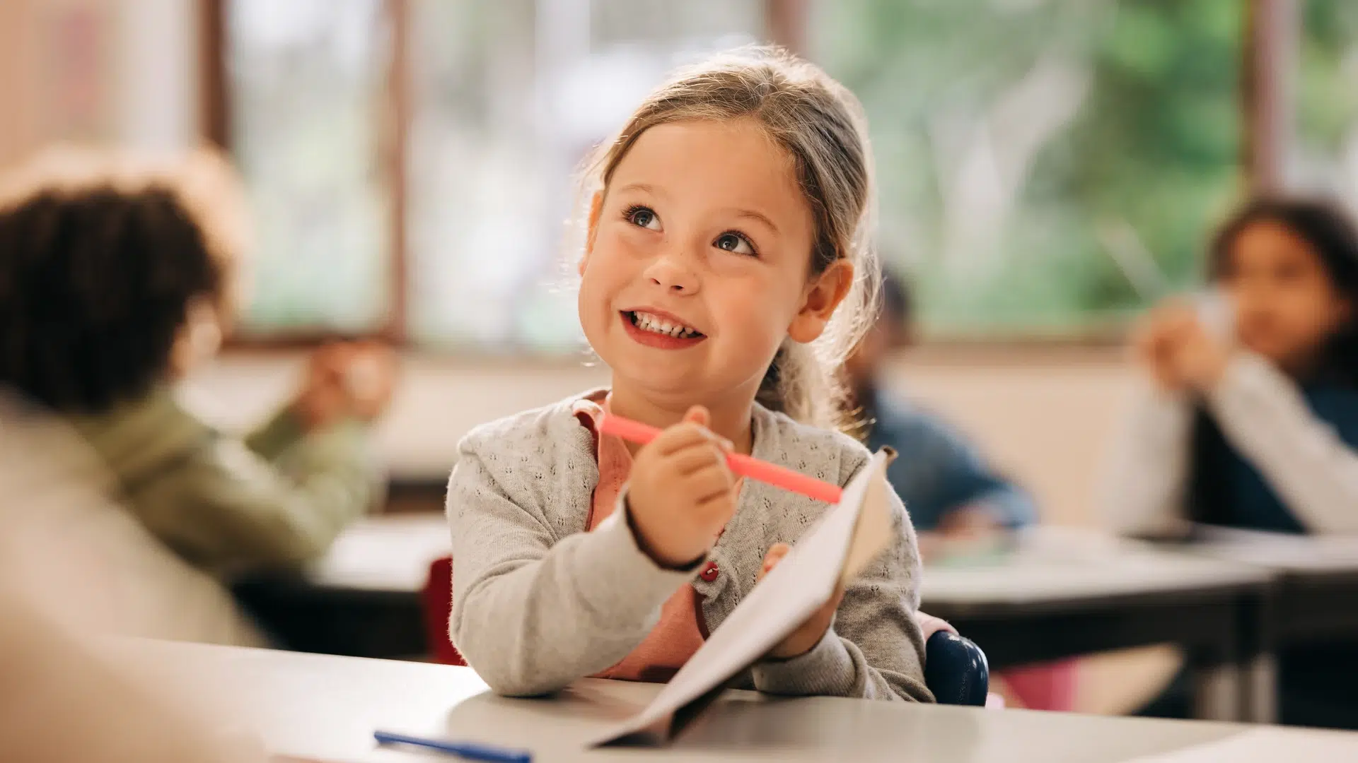 Enfant souriant en classe avec un crayon
